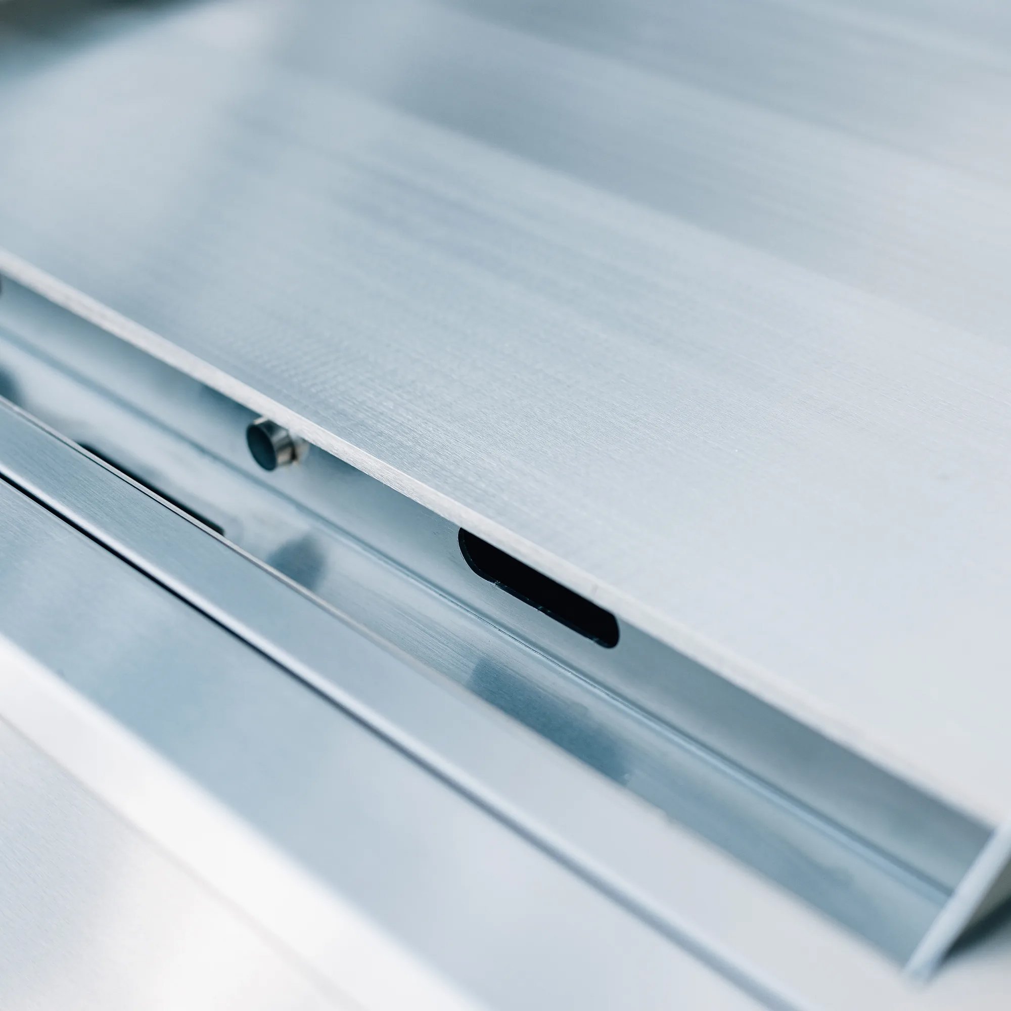 Close-up of the full-width stainless steel drip tray and grease drain slot on the Summerset 30-inch Griddle Pro built-in gas griddle