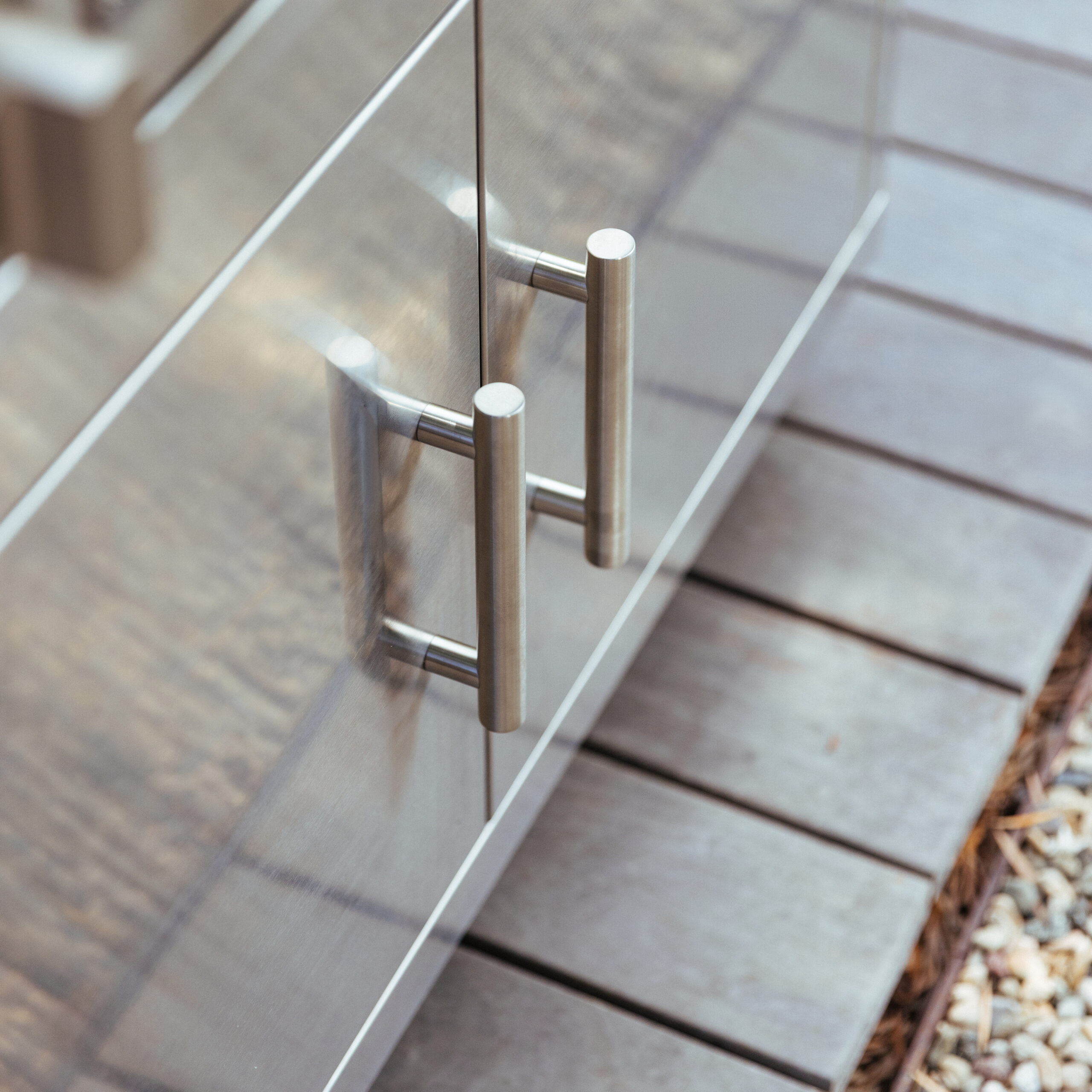 Close-up of the stainless steel double door pull handles on a Summerset grill cart, mounted on an outdoor patio