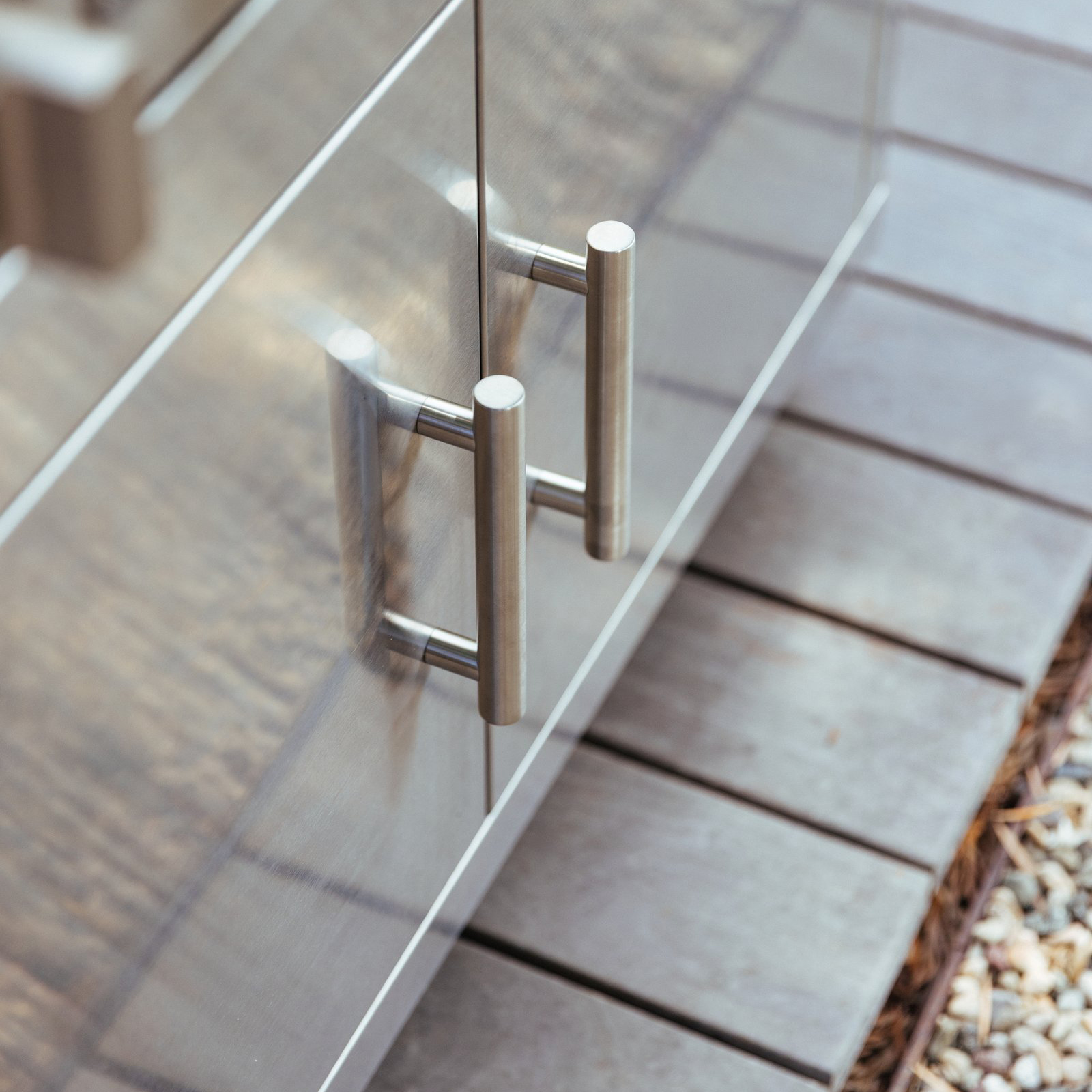 Close-up of the stainless steel double door pull handles on a Summerset grill cart, mounted on an outdoor patio